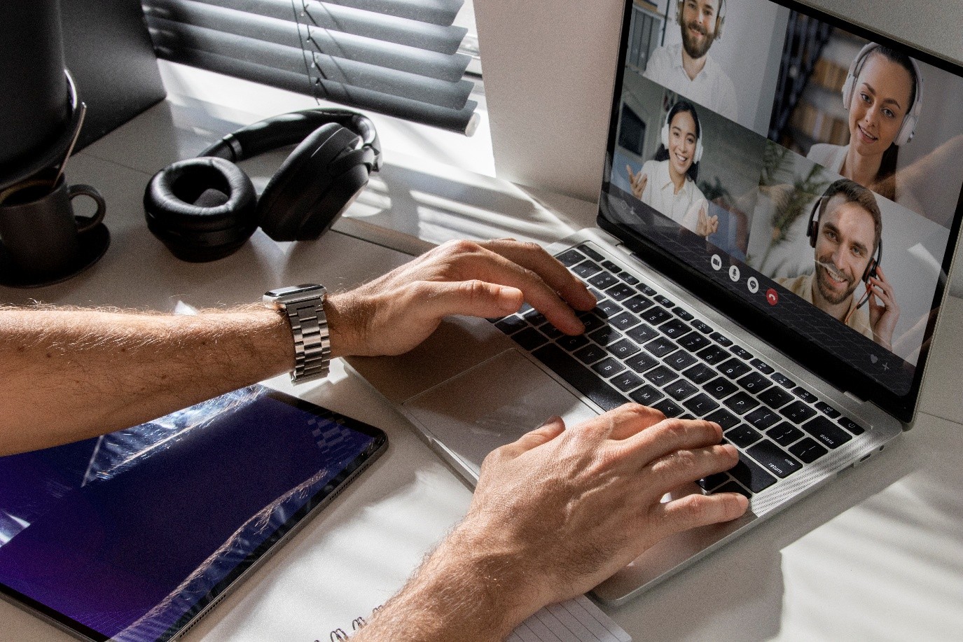 Person typing on a laptop during a Microsoft Teams video call with four hybrid colleagues wearing headsets